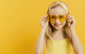 Красивая девочка блондинка в очках в форме сердца на желтом фоне