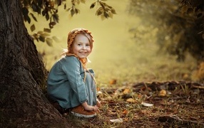 Красивая улыбающаяся девочка сидит под деревом