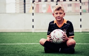 Мальчик футболист сидит на траве с мячом