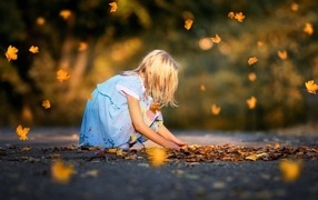 Девочка в платье играет с листьями на дороге