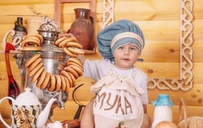 Маленький мальчик повар с продуктами и самоваром на столе