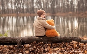 Маленький мальчик с игрушкой сидят на колоде у озера осенью