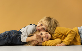 Маленькие брат и сестра лежат на полу на желтом фоне