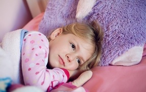 Маленькая кареглазая девочка лежит в кровати 