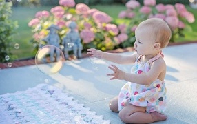 Маленькая девочка ловит мыльный пузырь