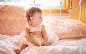 Маленькая девочка в платье сидит на кровати