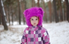 Маленькая девочка в меховой шапке в лесу зимой