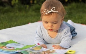 Маленькая девочка с книгой на белом покрывале