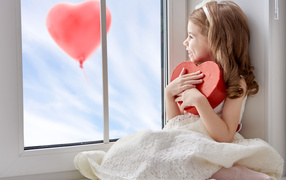 Маленькая девочка с коробкой в форме сердца сидит у окна