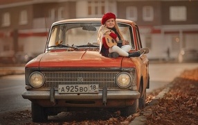 Маленькая девочка с гитарой сидит на красном автомобиле осенью