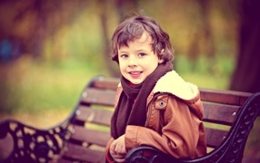 Маленький улыбающийся мальчик на лавке в парке