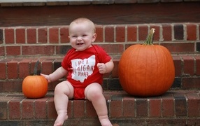 Маленький улыбающийся ребенок с тыквами на ступенях