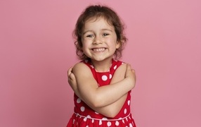 Улыбающаяся маленькая девочка в красном платье на розовом фоне