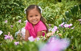 Улыбающаяся маленькая девочка сидит в цветах