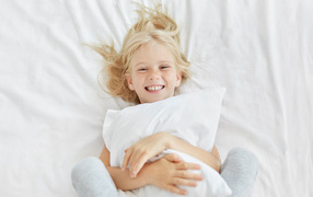 Улыбающаяся маленькая девочка с подушкой на кровати