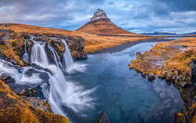 View of the river, waterfall and Kirkjufell mountain under the cloudy sky of Iceland