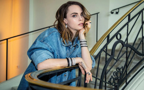 Актриса Кара Делевинь в джинсовой куртке стоит на лестнице