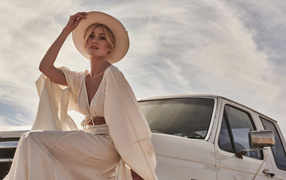 Actress Katherine McNamara in a white suit sits on a car