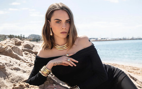 Кара Делевинь в черном платье лежит на песке