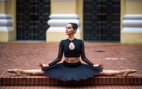 Девушка балерина в черном сидит на шпагате