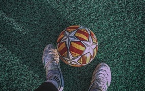 Футбольный мяч на зеленом поле с ногами футболиста