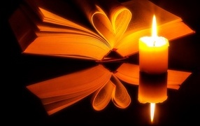 Открытая книга с зажженной свечой отражаются в черной поверхности