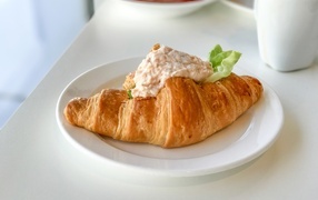Круассан с начинкой на белой тарелке на завтрак 