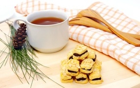 Печенье с чашкой чая и сосновой шишкой на столе