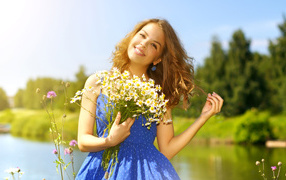 Милая улыбающаяся девушка с букетом ромашек у пруда летом
