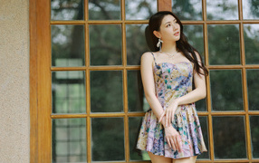 Длинноволосая азиатка в платье стоит у окна