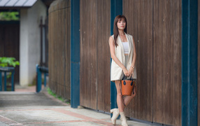 Скромная девушка азиатка с сумочкой стоит у стены