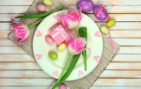 Пасхальные яйца с тюльпанами на тарелке на столе