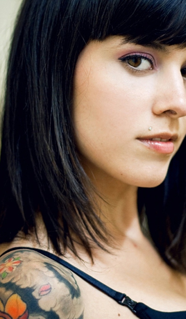 Девушка брюнетка с пирсингом в губе и татуировкой на плече