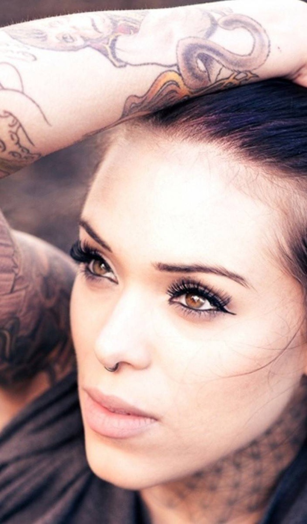 Девушка брюнетка с пирсингом в носу и татуировкой на руке