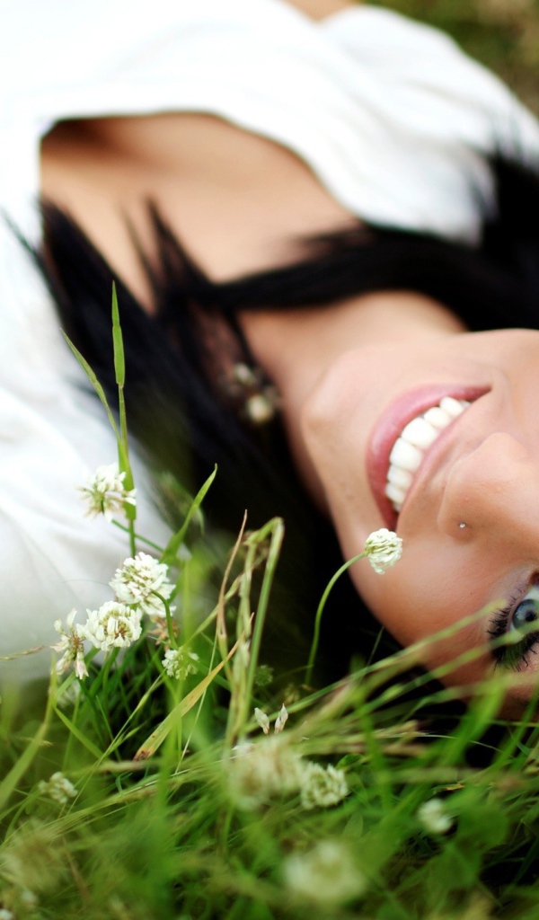 Девушка брюнетка с пирсингом в носу лежит в траве