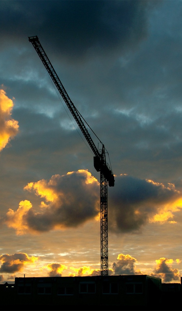 Стрелы кранов на стройке на фоне облаков