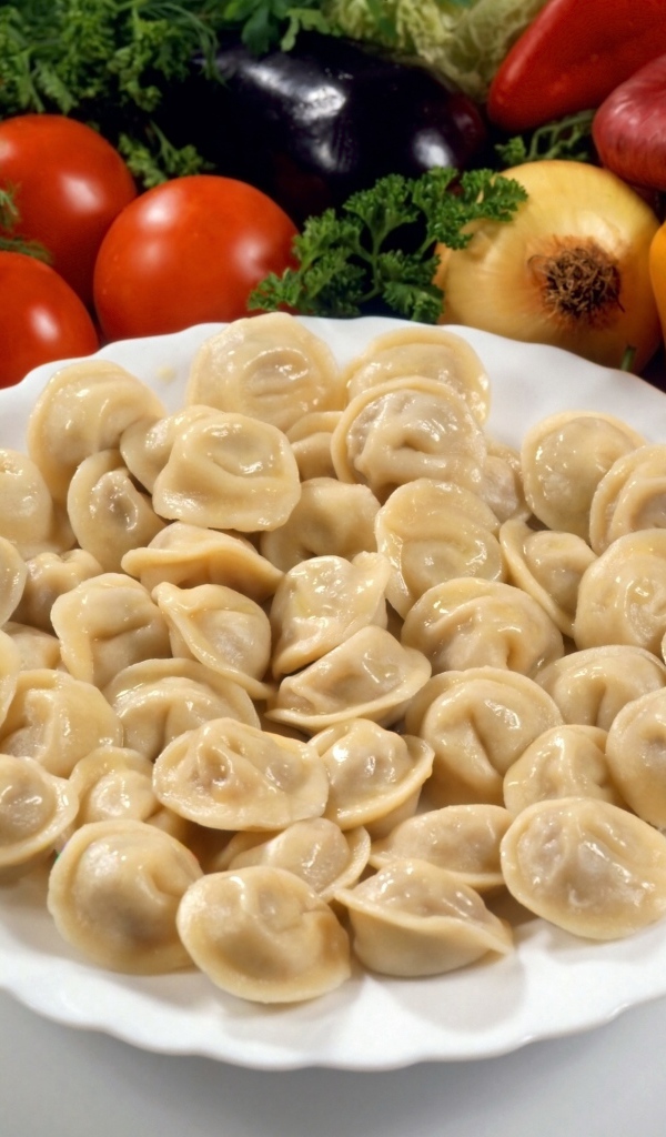 Пельмени на тарелке среди овощей