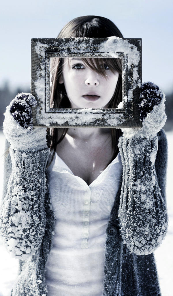 Девушка держит в руках фоторамку в снегу