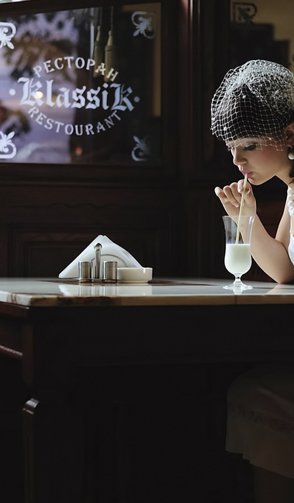 Девушка в белом платье пьет коктейль в ресторане