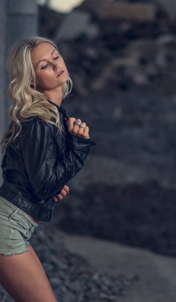 Блондинка в джинсовых шортах стоит у стены