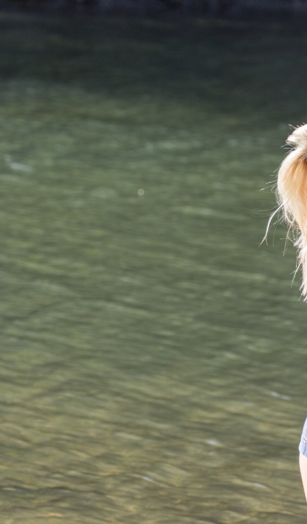 Блондинка в джинсовых шортах стоит на фоне воды