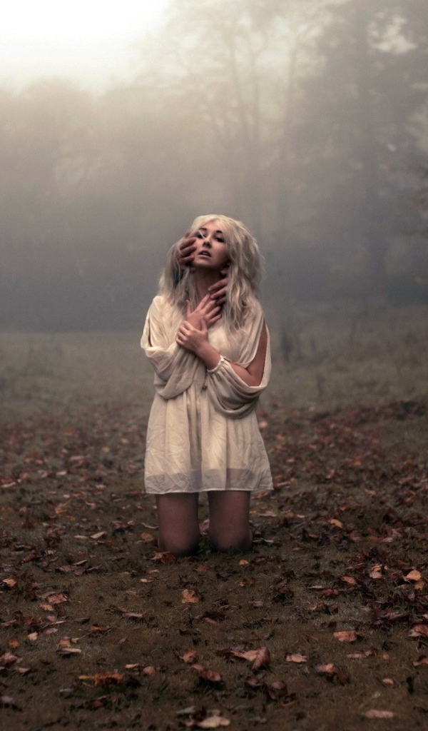 Блондинка в белом платье стоит на коленях среди леса