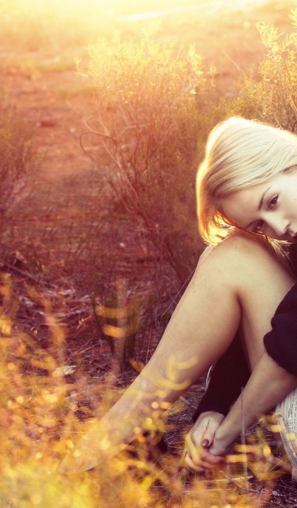 Блондинка сидит среди кустарников