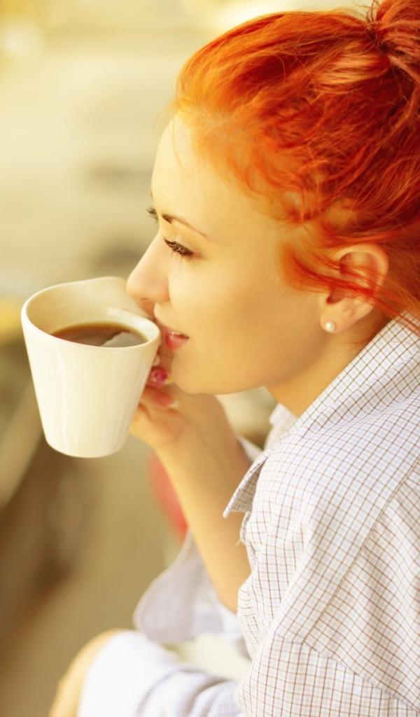 Ярко рыжая девушка в рубашке пьет кофе
