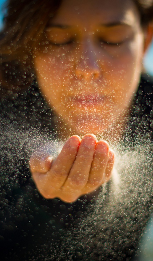 Девушка сдувает песок с руки