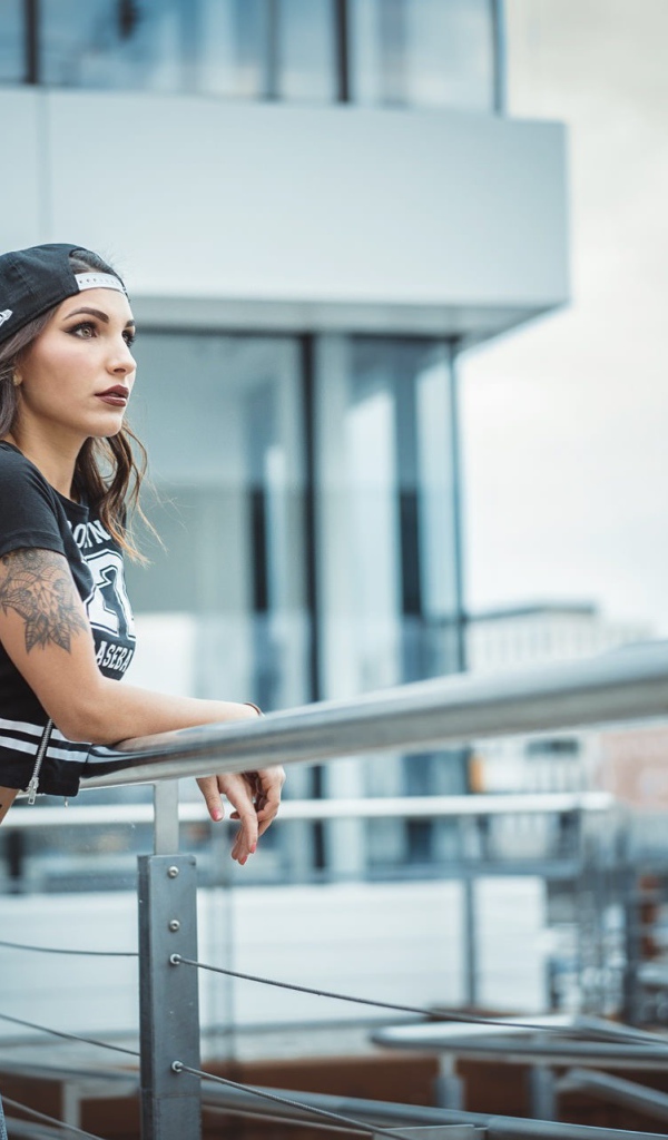 Девушка в кепке с тату смотрит на порт