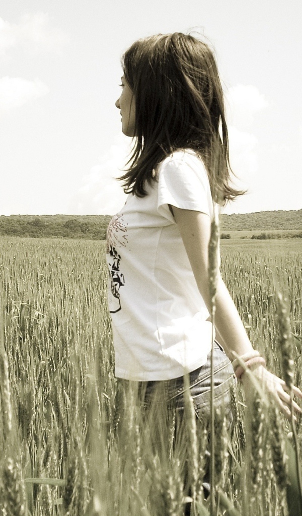 Девушка в белой футболке гуляет по пшеничному полю