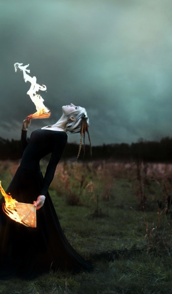 Девушка в черном платье играет с огнем