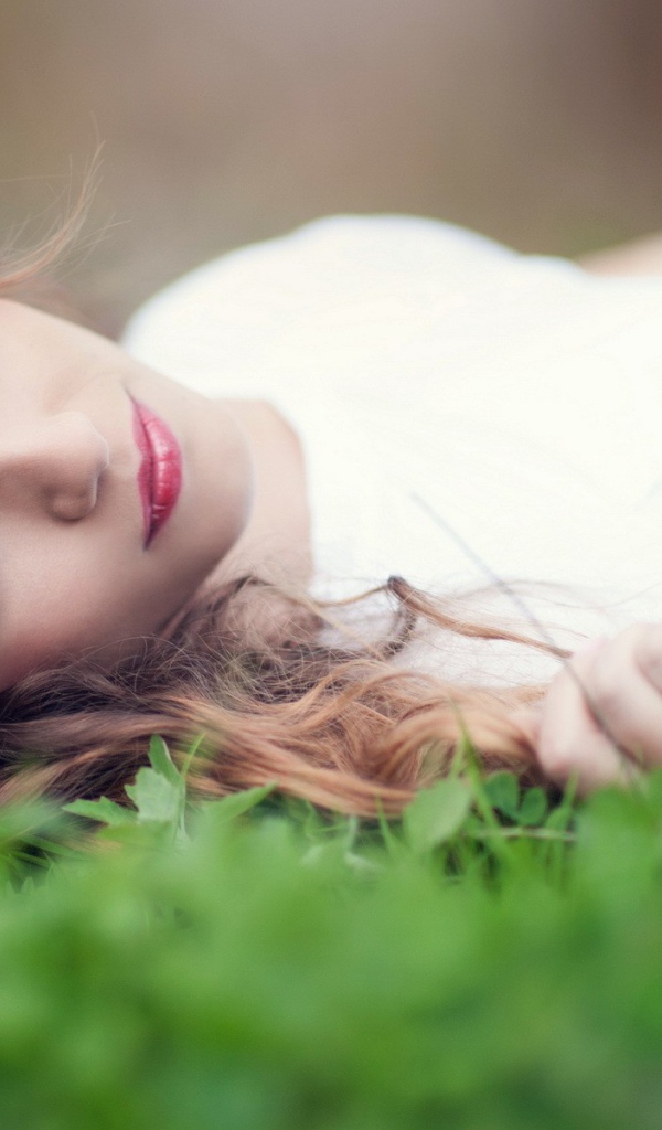 Девушка в белом платье с украшением в волосах лежит на траве