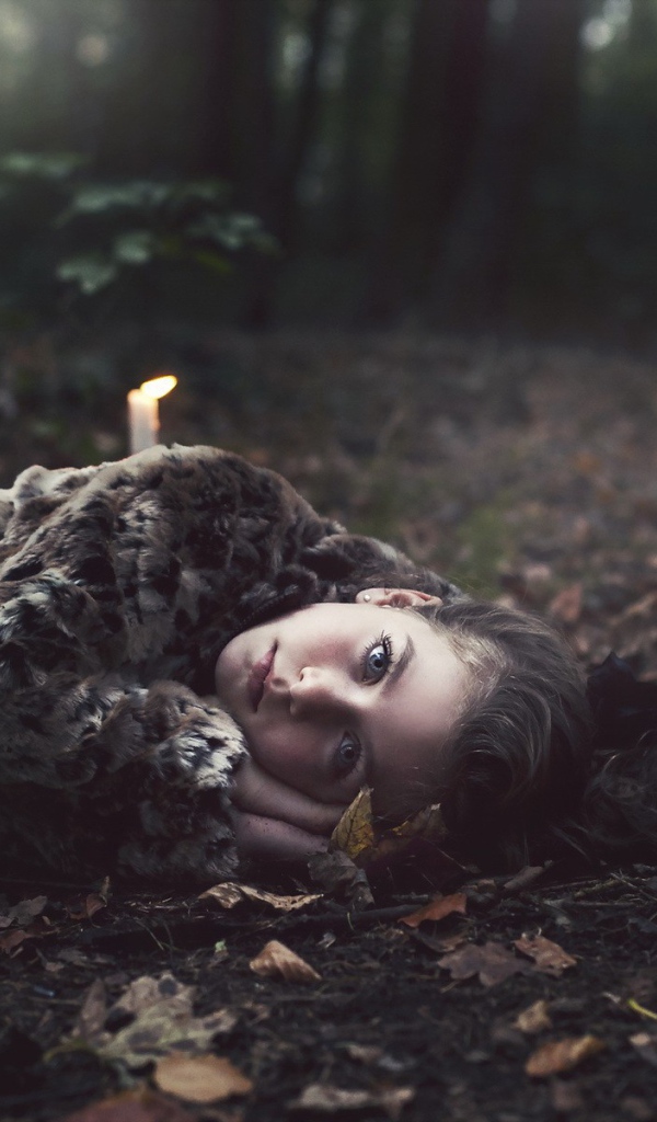 Девушка лежит среди свечей в лесу